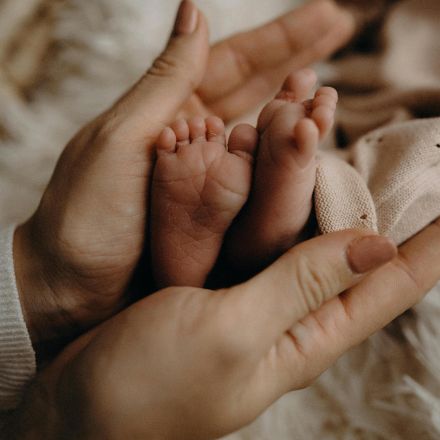 A close-up of a newborn's feet gently held by an adult's hands, symbolizing care and love.