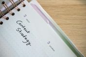 Top view of a notebook open to a day planner featuring 'Content Strategy' handwritten, lying on a wooden desk.